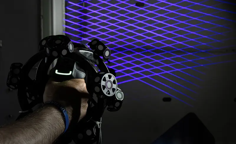Handheld 3D scanner head with blue laser lines streaming across a part